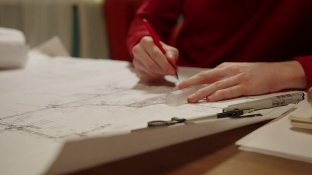 Young designer is sitting and drawing plan with ruler and compass, making notes in project. Architecture student is learning remotely at home in the evening.