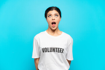 Young Russian volunteer girl isolated on blue background looking up and with surprised expression