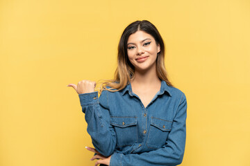 Young Russian girl isolated on yellow background pointing to the side to present a product