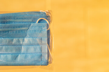 A few blue medical masks in a transparent bag on a blurred disposable warm orange background. Place for your text. Close-up