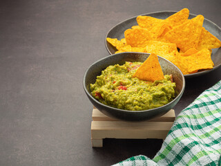 Fresh guacamole and tortilla chips on a plate placed on dark brown background with copy space for text. Top view. Concept of traditional Mexican foods and healthy fruits