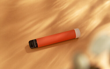 orange stick - disposable vaping device, electronic cigarette on a beige background. Flat lay, top view, minimal design with shadows of sunlight.