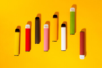 Layout of colorful disposable electronic cigarettes with shadows on a yellow background. The...