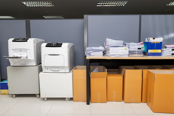 Printers, business documents stack on desk and cardboard boxes under desk.