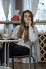 Young beautiful girl with long hair is drinking coffee in a cafe.