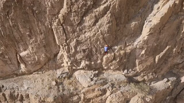 Rock Climber beginning ascent route at base of large Oman Rocky wall - Aerial Crane down Tracking shor