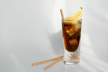 Glass of cola with ice, lemon and straw on white background