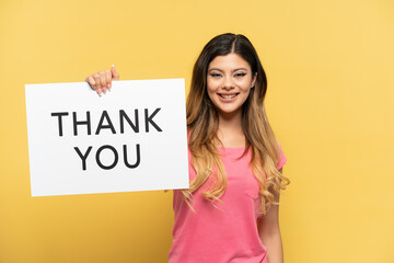 Young Russian girl isolated on yellow background holding a placard with text THANK YOU with happy expression