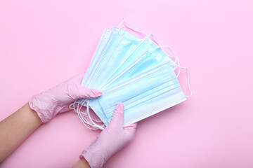 Female hands in protective gloves with medical masks on color background