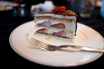 カフェの中の黒いテーブルクロスに置かれた白い皿の上のチョコレートがコーティングされたショートケーキ