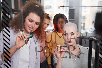 Girls writing slogans about women's rights at the transparent glass