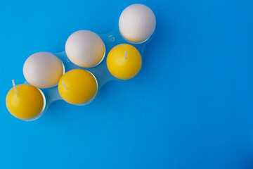 Three white chicken eggs and three yellow egg-shaped candles in a plastic stand. Easter card concept