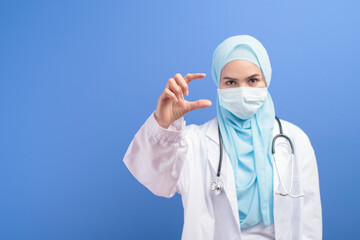 Female muslim doctor with hijab wearing a surgical mask over blue background studio.