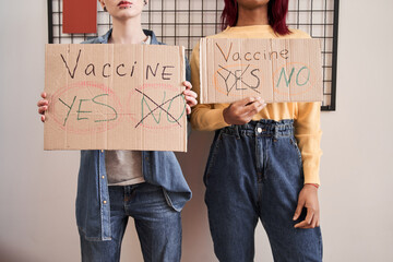 Girls showing to the camera cupboard posters about covid 19 crisis and vaccine