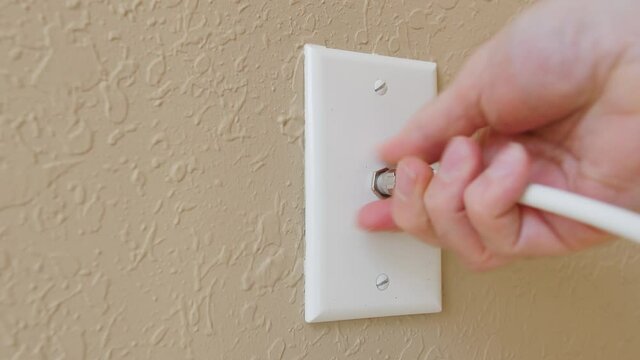 Male electrician disconnecting coax cable antenna wire from wall outlet. Coaxial connection for TV and high speed broadband internet. Television service installation.