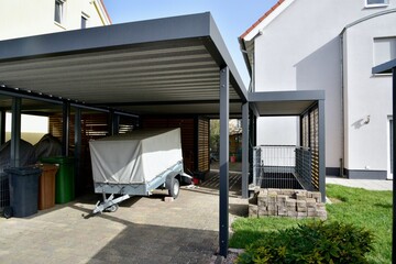 Neuer schwarzgrauer Carport aus beschichtetem Metall/Aluminium mit Flachdach an einem Wohnhaus