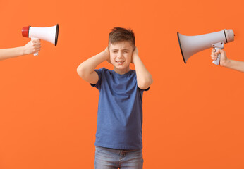 Hands with megaphones and little boy suffering from loud noise on color background