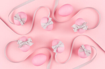 Elegant and girlish easter background - easter eggs with silver bow, wavy ribbons on pastel pink backdrop.