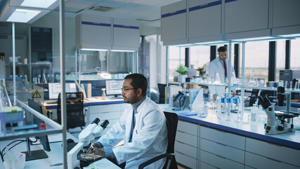 Medical Research Scientist Typing Sophisticated Coding on His Desktop Computer in a Biological Applied Science Research Laboratory. Multiethnic Lab Engineer in White Coat Conduct Experiments.