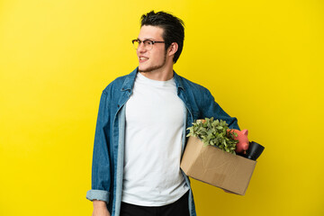 Russian Man making a move while picking up a box full of things isolated on yellow background...