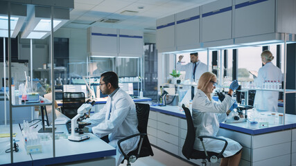 Team of Medical Research Scientists Conduct Experiments with Help of Microscope, Test Tubes, Micropipette and Writing Down Analysis Results on a Computer. Modern Biological Applied Science Laboratory.