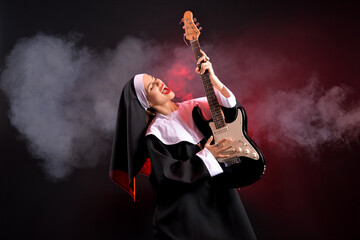 Young nun playing guitar on dark background