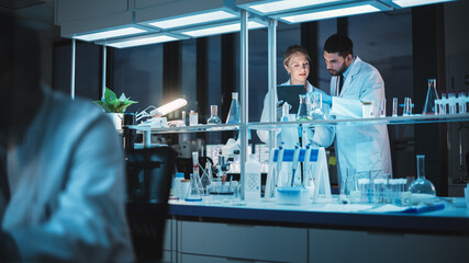 Female and Male Medical Research Scientists Have a Conversation While Conducting Experiments in a Petri Dish, Writing Analysis Results on a Tablet Computer. Modern Biological Science Laboratory.