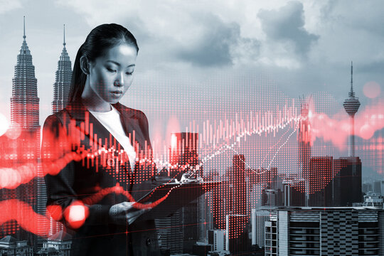 Attractive Asian trader in suit examine her notes to predict the market behavior based on historic data and stock market. Corporate finance fund and forex chart. Kuala Lumpur. Double exposure.