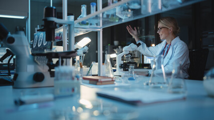 Medical Development Laboratory: Caucasian Female Scientist Analyzes Petri Dish Sample with use of...