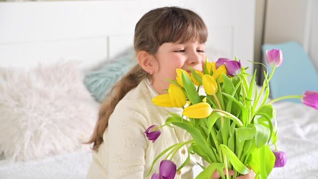 Smiling Little girl with a bouquet of bright tulips in her hands, she sniffs them and smiles. A gift for mom or grandmother on women's day. 8 March Women's Day concept. High quality FullHD footage
