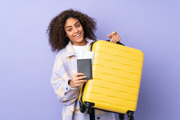 Fototapeta premium Young African American woman isolated on purple background in vacation with suitcase and passport