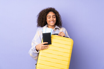 Young African American woman isolated on purple background in vacation with suitcase and passport