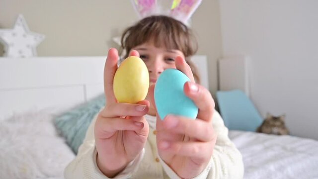 Smiling Little girl in rabbit ears is having fun, playing, jangles with colored Easter eggs. Chocolate eggs of different colors for Easter in the hands of a child. FullHD footage. slow-motion 