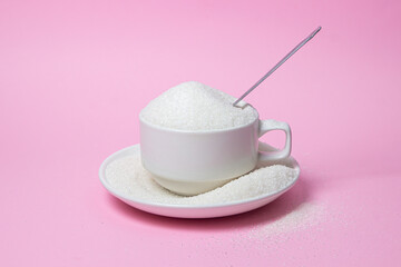 Excessive sugar intake. Sugar on a pink background. An overflowing cup of sugar.