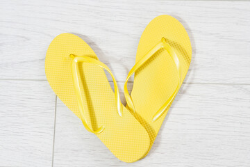 Yellow flip-flops on a white wooden background close up