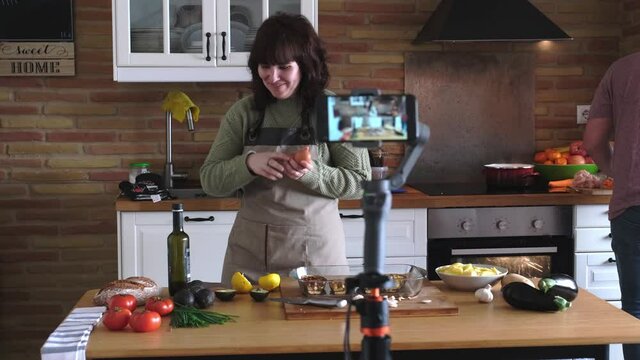 Young woman explaining how to cook guacamole to the camera and recording a video with her smartphone for her cooking channel. Content creator and influencer.
