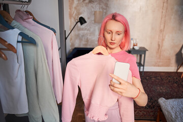 Woman with pink hair shooting with hanger with clothes ​at her smartphone