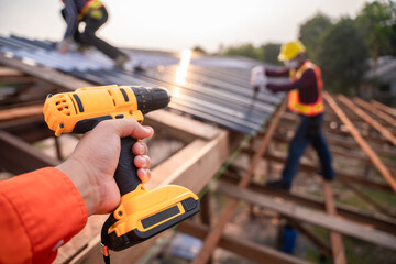 Selective focus Roofing tools, Roofer worker holding electric drill used on new roofs with Metal Sheet at construction site.