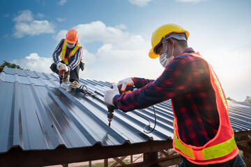 Two Roofer worker safety wear using air or pneumatic nail gun and installing on new roof metal...