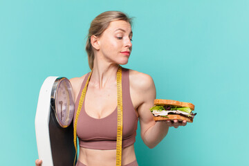 young pretty sport woman doubting or uncertain expression and holding a scale and a sandwich