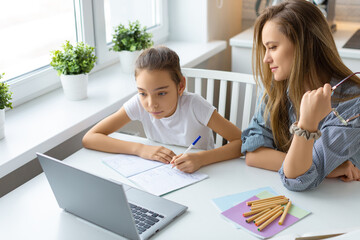 Teenage girl doing homework online at home. Mom closely monitors the correctness of homework.