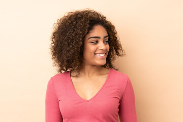 Young African American woman isolated on beige background looking to the side and smiling