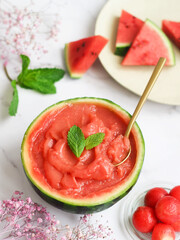 A fresh homemade watermelon sorbet in its shell decorated with mint leaves, golden spoon inside with its ball and its pieces. A perfect refreshing treat for summer. It's actually healthy, paleo&vegan