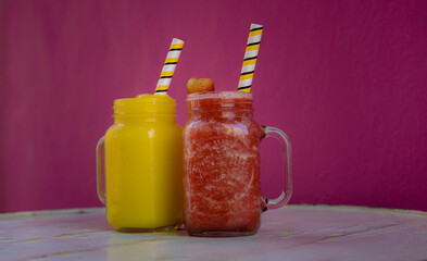 Mango and strawberry smoothie on a table, background a pink wall