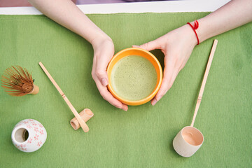 Woman holding cup of matcha latte while sitting at the kitchen at the table