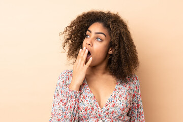 Fototapeta na wymiar Young African American woman isolated on beige background yawning and covering wide open mouth with hand