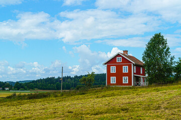 Red Swedish farmhouse on a hill. A cozy summer landscape with a countryside house