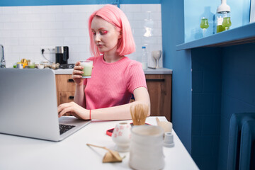 Girl with pink hair drinking her morning matcha tea and working at her laptop