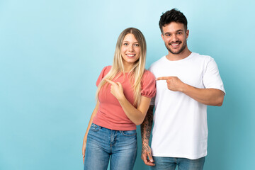 Fototapeta premium Young caucasian couple isolated on blue background pointing finger to the side and presenting a product