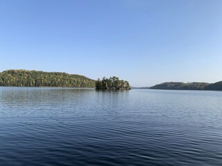 Beautiful lake scenery on a calm summer day with islands in the horizon. The sky is blue and there are no clouds. Concepts of summer holiday and peace of mind.